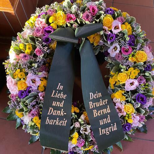 Farbenfroher Trauerkranz mit Rosen und Chrysanthemen, geschmückt mit Schleifenbotschaft „In Liebe und Dankbarkeit“, gestaltet vom erfahrenen Bestatter in Berlin.