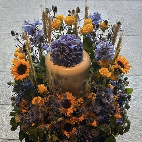 Elegante Urne, umgeben von einem Blumenarrangement aus Sonnenblumen, Hortensien und Rosen, liebevoll gestaltet von Bestatter Berlin für eine würdevolle Abschiednahme.