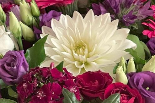 Detailreiches Blumengesteck mit Dahlien, Rosen und Gerbera in kräftigen Rosa-, Rot- und Lilatönen, gestaltet von Ihrem Bestatter in Berlin für eine stilvolle Abschiednahme.