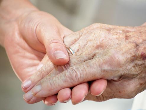 Nahaufnahme zweier Hände, eine ältere und eine jüngere, die sich liebevoll halten.